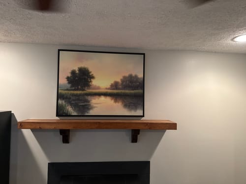 Reviewer's The Journey Canvas Art in a floating black frame, mounted above a wooden fireplace mantel.