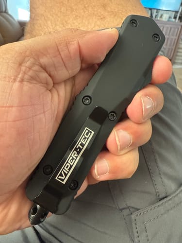 Customer's hand holding the closed black Hornet OTF knife, showing the handle texture and pocket clip.