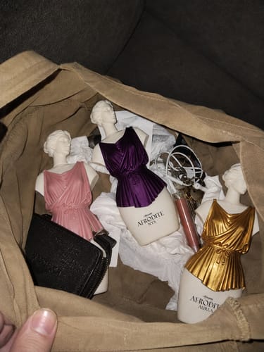 Customer's Kit Afrodite perfume bottles in pink, purple, and gold inside a brown bag with personal items.