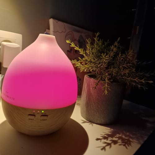 Customer's Nimbus 2.0 aroma diffuser in light wood, emitting a soft pink LED light next to a small potted plant.