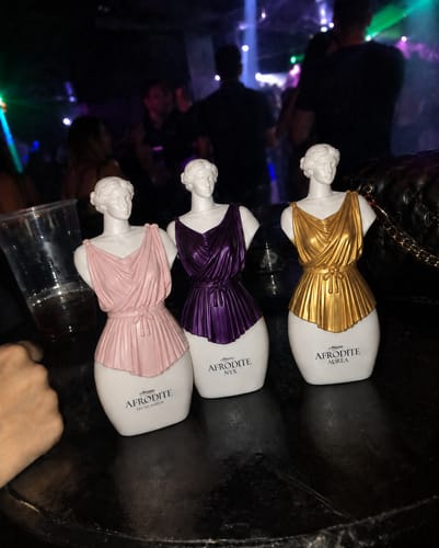 Customer's three Kit Afrodite fragrance bottles shaped like classical busts on a nightclub table.