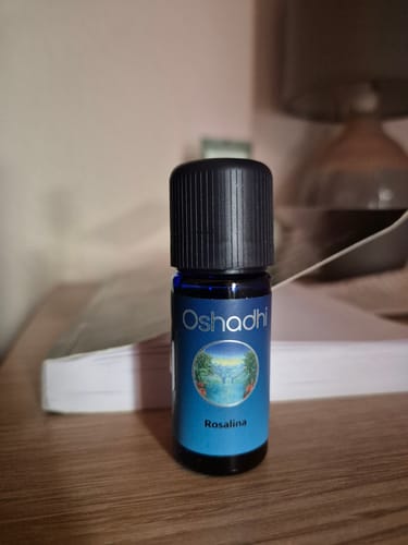 Customer's Oshadhi Rosalina ätherisches Öl, eine kleine blaue Glasflasche mit schwarzem Deckel auf einem Holztisch.