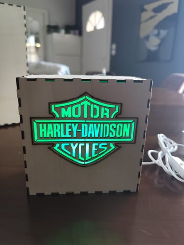 Customer's AtomStack A20 Pro V2 laser-engraved wooden box with glowing green Harley-Davidson logo on a table.