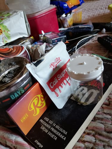 Customer's clear container for THC-A 29% Flower White Truffle, resting on a table with smoking supplies.