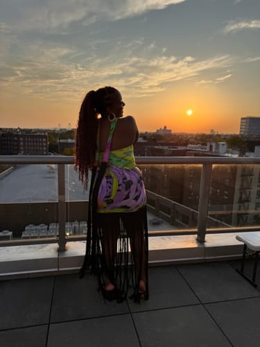 Reviewer's Naked Print Fringe Tube Dress, showing back view and long black fringe while posing on a rooftop at sunset