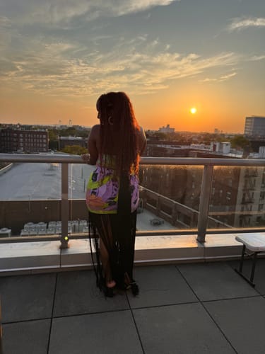 Reviewer's Naked Print Fringe Tube Dress, back view against a colorful sunset cityscape from a rooftop