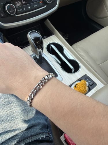 Customer's stainless steel Cuban Link Bracelet on wrist, shown from inside a vehicle.