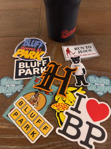 Customer's pile of assorted custom 3-inch stickers on a wooden surface next to a cup.