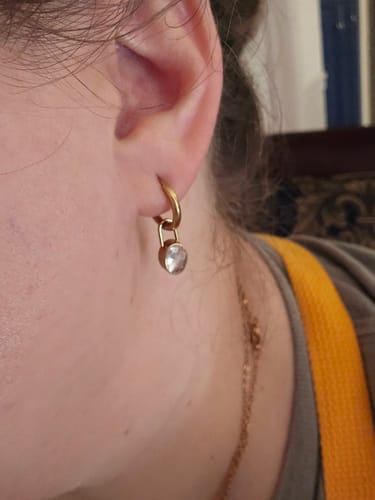 Customer's gold Diamond Lock earring with a small dangling zirconia charm worn on the earlobe.