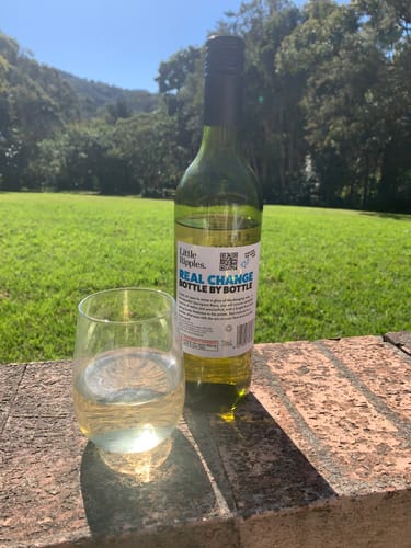 Reviewer's Little Ripples wine bottle and a filled glass sitting on a brick ledge in a grassy outdoor setting.