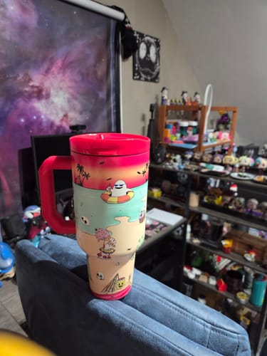 Customer's Thicc Buddy 50oz Sunscream mug with a colorful beach-themed graphic, resting on a blue chair.