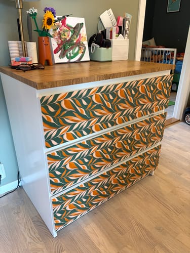 Anmelderens Boho Leaves kontaktplast montert på skuffene til en kommode med grønt, oransje og hvitt bladmønster.