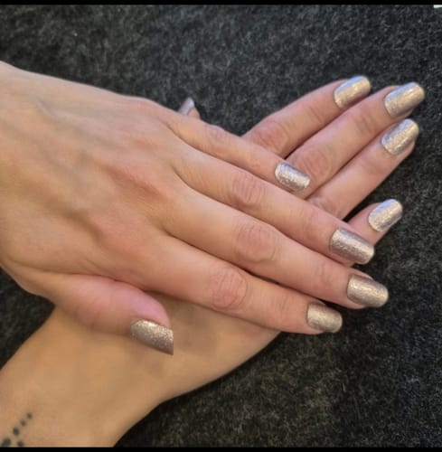 Reviewer's hands displaying elegant rosé-colored Elegant Glow UV gel nail wraps on a dark textured background.