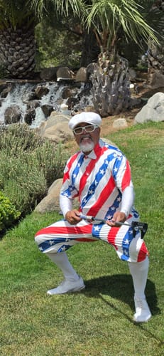 Reviewer in a red, white, and blue patriotic Men's American President Day Polo holding a golf club on a grassy course.