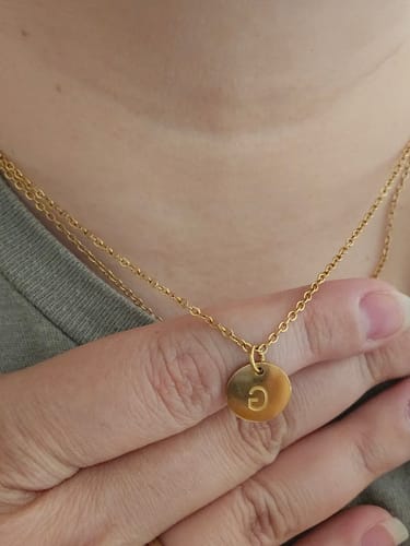 Customer's gold Aura Initial Necklace worn on the neck, featuring a round pendant with the letter G.