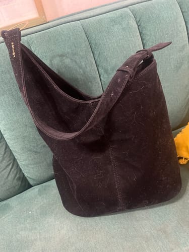 Customer's black fake suede asymmetrical shoulder bag resting on a green textured sofa.