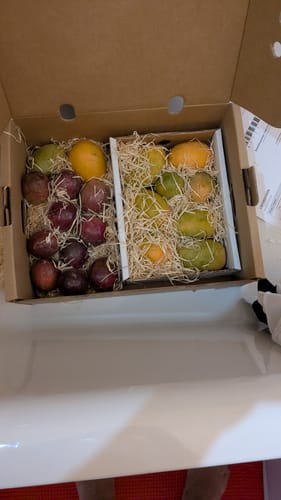 Kunden-Foto der Bio Passionsfrüchte und Mangos von Julian, verpackt in einer Versandbox mit Holzwolle.