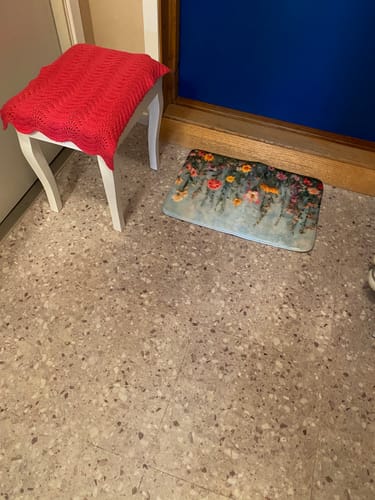 Customer's Sahara beige selvklebende fliser installert på et gulv ved siden av en krakk med et rødt teppe.