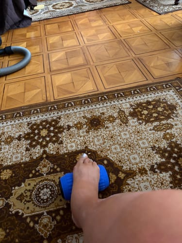 Customer's foot resting on a blue Vibráló Masszázshenger on a patterned rug.