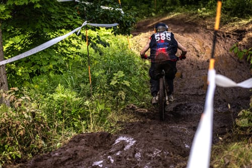 Customer's Highroller Cargo Trousers in shadow black being worn by a rider on a muddy mountain bike trail.
