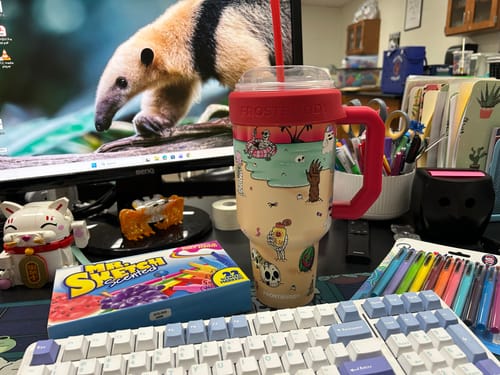 Reviewer's Thicc Buddy mug with a graphic design, sitting on a desk next to markers and a computer monitor.