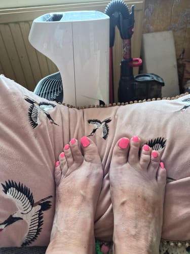 Customer's feet wearing bright pink Electric Pink Toes gel polish while resting on a bird-patterned pillow.