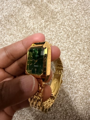 Customer's gold-tone Clarine watch with a green dial, held by a hand to show a scratch on the glass surface.
