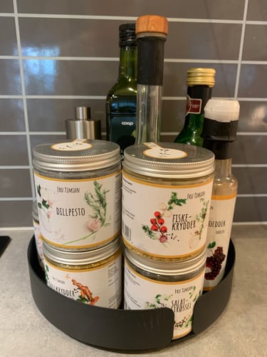 Customer's matt sort Snurrebrett fylt med krydderkrukker og flasker på kjøkkenbenken.