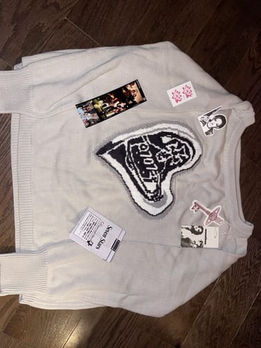 Customer's off-white 707 FLAME KNIT SWEATER laid flat with several included decorative stickers and tags on top.