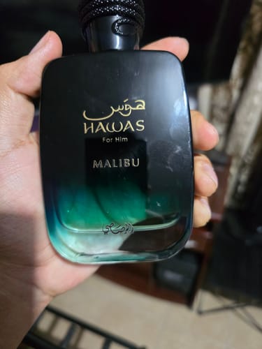 Customer's hand holding the dark-to-teal gradient glass bottle of Rasasi Hawas Malibu perfume.