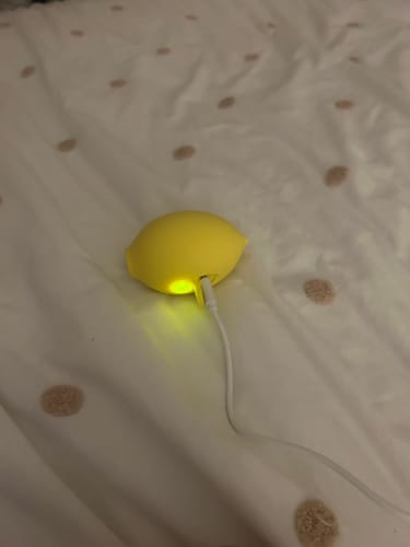 Customer's yellow Lem clitoral massager plugged into a charging cable on a patterned bed sheet