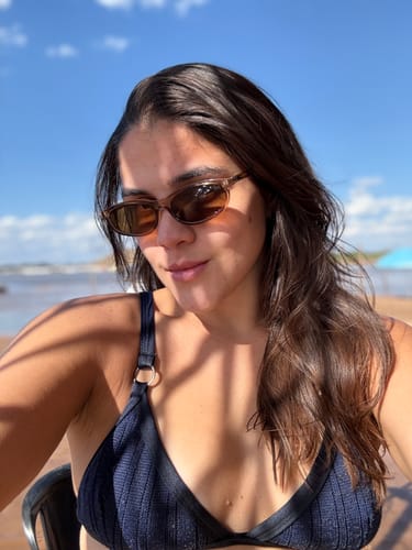 Customer's oval Cumbuco sunglasses being worn by a person at the beach.