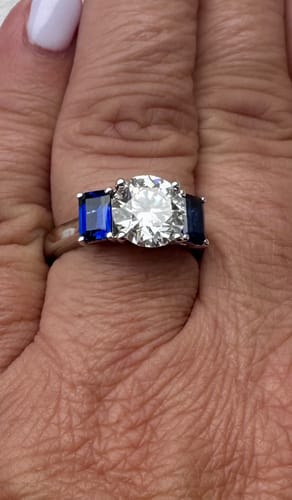 Customer's Customization semi mount ring with a round center stone and blue emerald-cut side stones on a finger.
