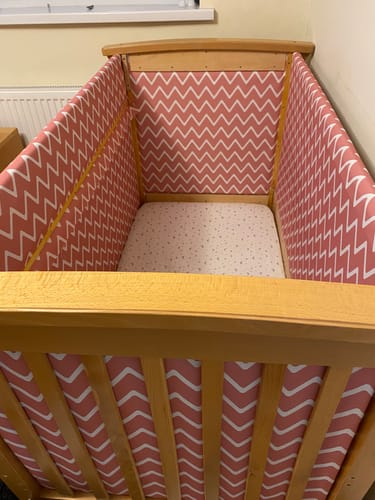 Reviewer's pink chevron print fabric lining a wooden baby cot to pad the interior.