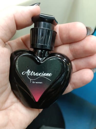 Customer's Attracione Sensual perfume held in a hand, showing the heart-shaped black bottle with white branding.