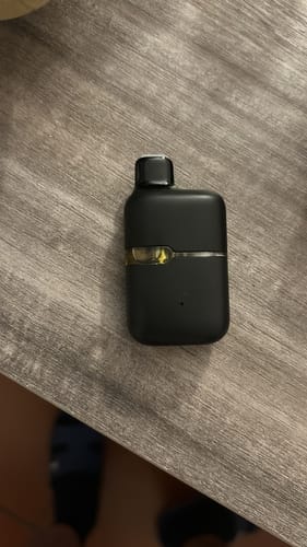 Reviewer's black ROLLZ THC-A Vape, compact and rectangular, resting on a gray wooden surface.