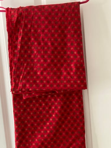 Customer's Holiday Twinkle Christmas cotton fabric hanging on a rack, showing red material with metallic snowflakes.
