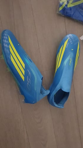 Customer's pair of blue and yellow Adidas F50 Laceless Elite FG football boots on a wooden floor.