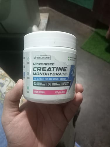 Reviewer's hand holding a white Wellcore Creatine Monohydrate tub with a Fruit Fusion label.