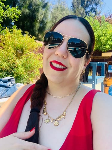 Customer's Collar Charms Marino worn as a golden layered necklace with charms, outdoors in a red top.