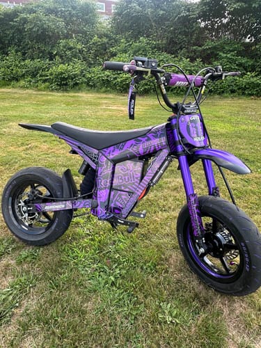 Reviewer's purple electric bike with custom decals parked on grass, highlighting the rear shock cover installation.