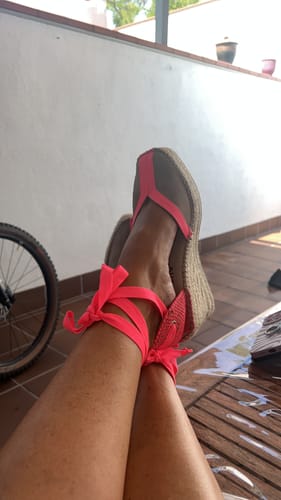 Customer's Alpargata Mara Fucsia wedges with neon pink ribbon ties, shown resting on a porch.