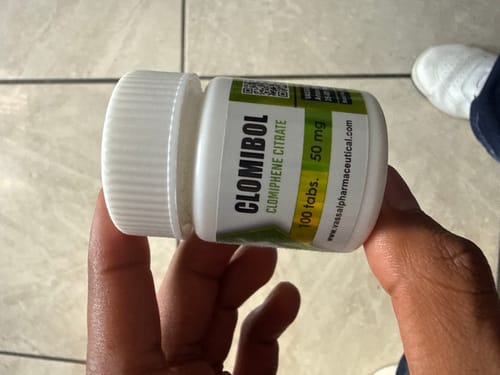 Customer's hand holding a white bottle of Clomibol Clomiphene Citrate tablets from the post ciclo pack.