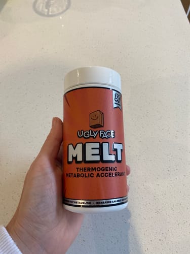 Reviewer's hand holding a bottle of UGLYFACE MELT thermogenic supplement against a white countertop