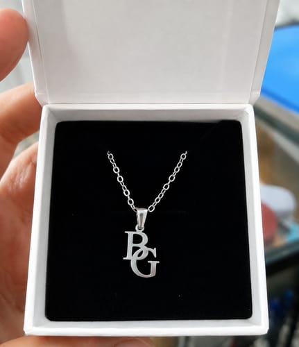 Customer's personalisierte Monogramm-Kette in einer geöffneten, weißen Schmuckschachtel auf schwarzem Samt.