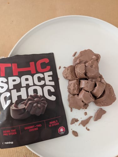Customer's geschmolzene THC SpaceChoc Schokolade auf einem weißen Teller neben der schwarzen Originalverpackung.