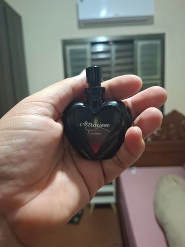 Customer's hand holding a black heart-shaped perfume bottle, the Attracione Sensual fragrance, in an indoor setting.