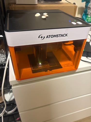 Customer's AtomStack P1 Laser Engraver with an orange safety shield, in operation on a white surface.