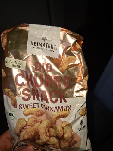 Kundenfoto der Bio Churro Snack Packung in der Hand, zeigt die golden glänzende Verpackung mit Zimtgebäck.