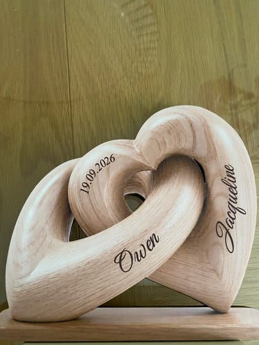 Customer's personalized wooden Interlocked Hearts plaque, engraved with names and a date, sitting on a base.